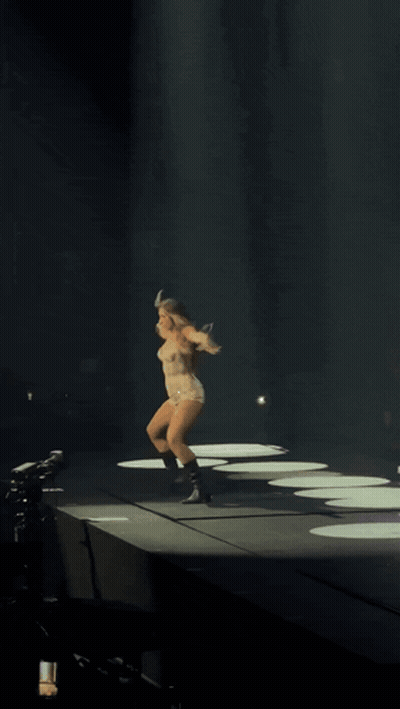 A Woman Is Dancing On A Stage With Her Arms Outstretched In The Dark GIF