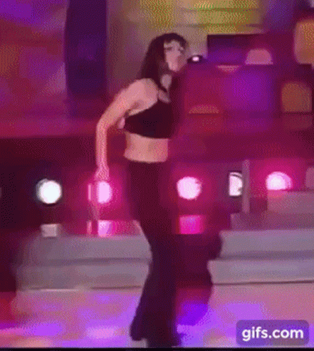A Woman Is Dancing On A Stage With Purple Lights Behind Her GIF