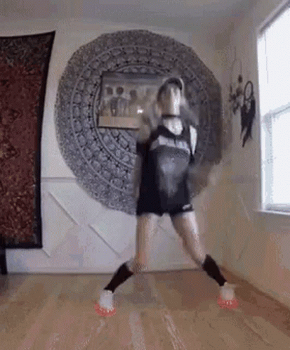 A Woman Is Dancing On A Wooden Floor In A Room With A Mandala On The Wall . GIF