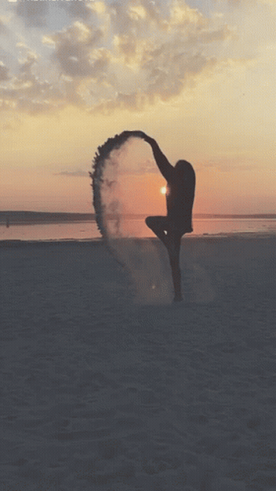 A Woman Is Dancing On The Beach At Sunset With Smoke Coming Out Of Her Feet GIF