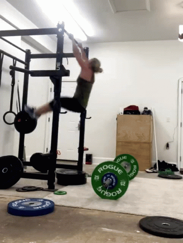 A Woman Is Doing A Pull Up In A Gym With A Barbell That Says Rogue On It GIF
