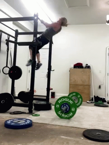 A Woman Is Doing A Pull Up In A Gym With A Barbell That Says Rogue On It GIF