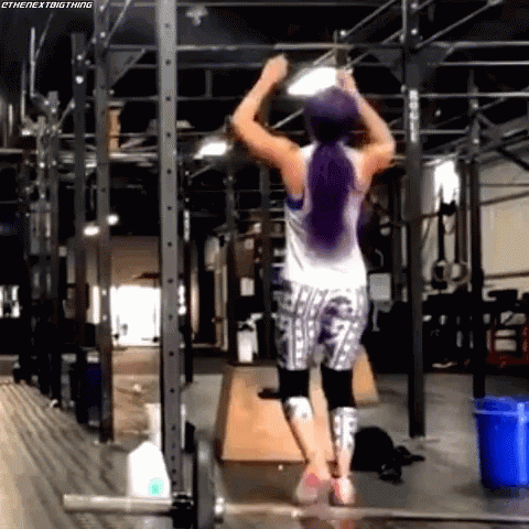 A Woman Is Doing A Pull Up In A Gym With A Blue Bucket In The Background . GIF