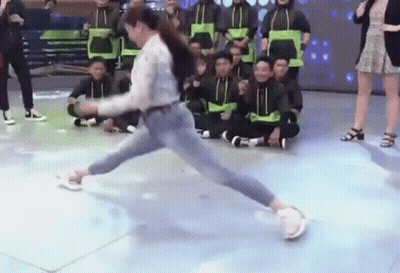 A Woman Is Doing A Trick On A Dance Floor In Front Of A Group Of People Sitting On The Floor . GIF