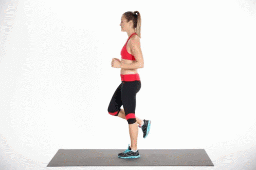 A Woman Is Doing A Workout On A Yoga Mat While Standing On One Leg . GIF