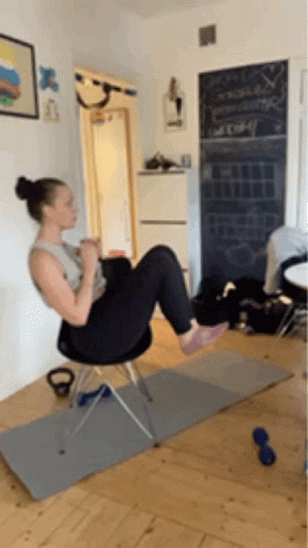 A Woman Is Doing Exercises On A Chair In A Living Room GIF