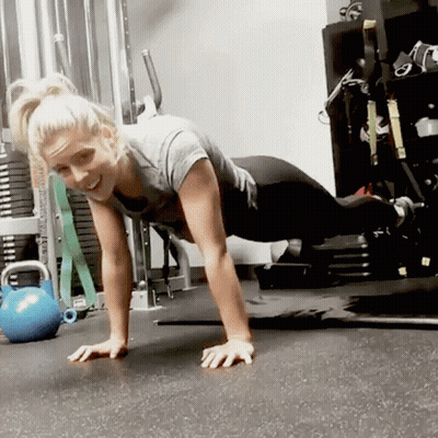 A Woman Is Doing Push Ups In A Gym With A Blue Kettlebell In The Background GIF