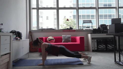 A Woman Is Doing Push Ups In Front Of A Red Couch And A Sign That Says " No Smoking " GIF