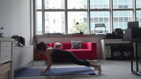 A Woman Is Doing Push Ups On A Yoga Mat In Front Of A Red Couch And A Sign That Says Do Not Enter GIF