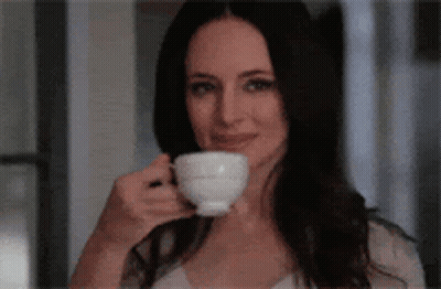 A Woman Is Drinking A Cup Of Coffee While Smiling . GIF
