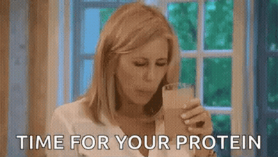 A Woman Is Drinking A Protein Shake In Front Of A Window While Talking On A Cell Phone . GIF