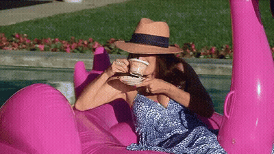 A Woman Is Drinking Coffee While Sitting On A Pink Flamingo Float In A Pool . GIF