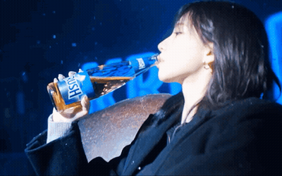 A Woman Is Drinking From A Bottle That Says Rush On It GIF