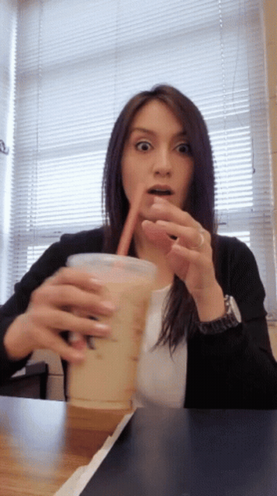 A Woman Is Drinking From A Cup That Says ' Iced Coffee ' On It GIF