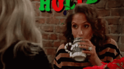 a woman is drinking from a mug while sitting at a table .