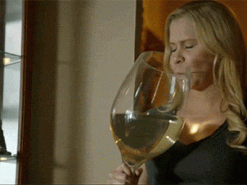 A Woman Is Drinking From A Very Large Glass Of Wine GIF