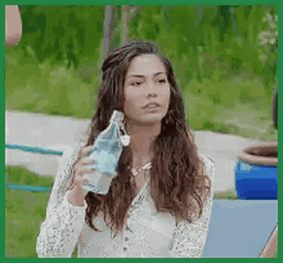 A Woman Is Drinking Water From A Bottle While Sitting On A Bench . GIF
