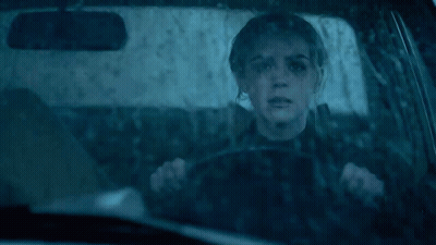 A Woman Is Driving A Car In The Rain With A Reflection Of Her Face In The Windshield GIF
