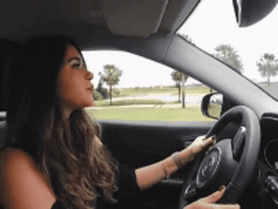 A Woman Is Driving A Car On A Road GIF