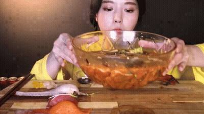 A Woman Is Eating A Bowl Of Food With Chopsticks GIF