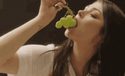 A Woman Is Eating A Bunch Of Grapes With A Tattoo On Her Arm GIF