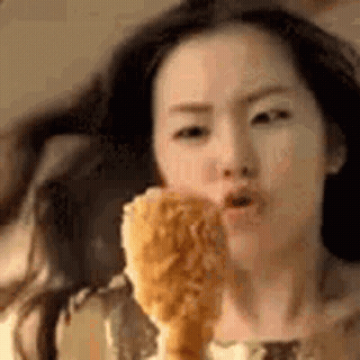 A Woman Is Eating A Fried Chicken Leg In A Close Up . GIF