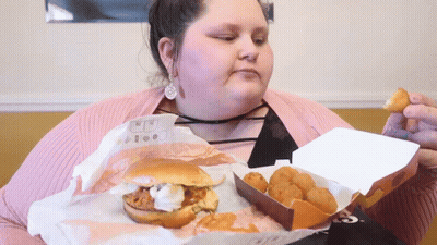 A Woman Is Eating A Hamburger And Chicken Nuggets From A Box GIF