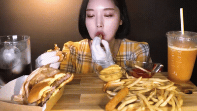 A Woman Is Eating A Hamburger And French Fries At A Table With A Drink That Says Tropical GIF