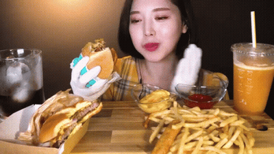 A Woman Is Eating A Hamburger , French Fries And A Drink . GIF