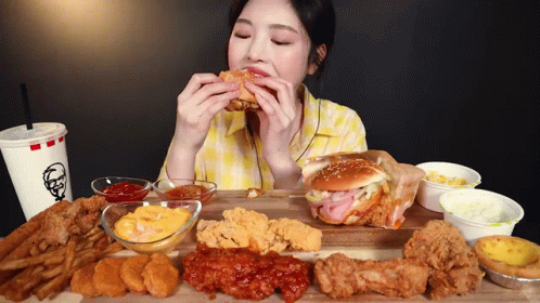 A Woman Is Eating A Hamburger On A Cutting Board With A Kfc Drink GIF