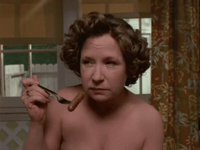 A Woman Is Eating A Hot Dog With A Fork . GIF
