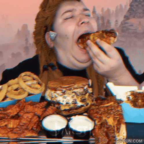 A Woman Is Eating A Large Amount Of Food Including A Hamburger Onion Rings And Wings GIF