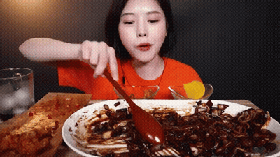 A Woman Is Eating A Large Plate Of Food With A Spoon . GIF