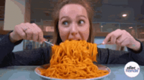 A Woman Is Eating A Large Plate Of Spaghetti With A Fork And Knife GIF