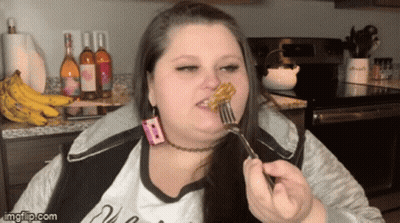 A Woman Is Eating A Piece Of Food With A Fork In Front Of Bottles Of Wine And Bananas GIF