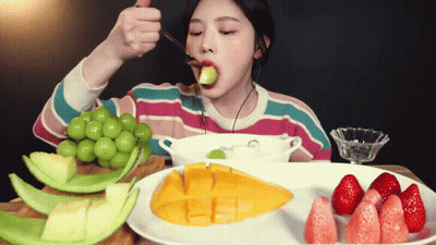 A Woman Is Eating A Piece Of Fruit With A Spoon In Her Mouth GIF