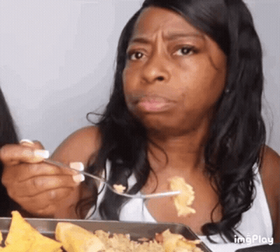 A Woman Is Eating A Plate Of Food With A Fork And Spoon . GIF
