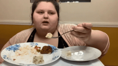 A Woman Is Eating A Plate Of Food With A Fork And Spoon GIF