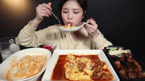 A Woman Is Eating A Plate Of Food With A Spoon And Fork GIF