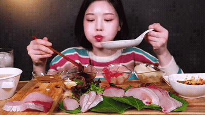 A Woman Is Eating A Plate Of Food With Chopsticks And A Spoon GIF