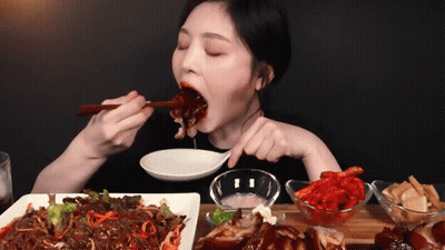 A Woman Is Eating A Plate Of Food With Chopsticks And A Spoon GIF