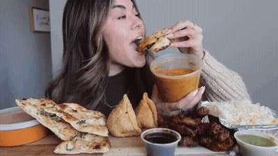 A Woman Is Eating A Sandwich And Holding A Cup Of Soup GIF