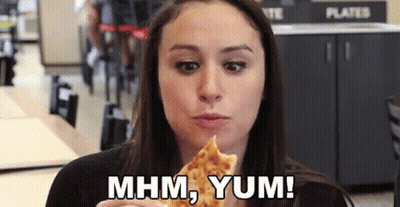 A Woman Is Eating A Slice Of Pizza In A Restaurant And Saying Mhm Yum . GIF