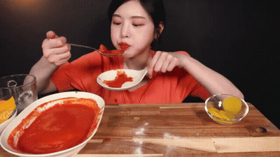 A Woman Is Eating A Spoonful Of Sauce From A Bowl GIF