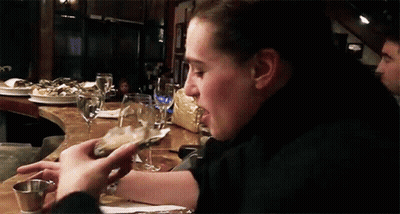 A Woman Is Eating An Oyster While Sitting At A Table In A Restaurant GIF