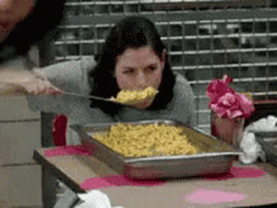 A Woman Is Eating Food From A Tray With A Spoon GIF
