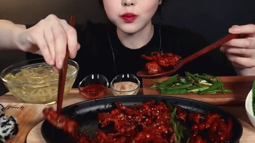 A Woman Is Eating Food With Chopsticks And A Spoon GIF