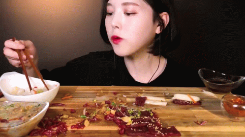 A Woman Is Eating Food With Chopsticks On A Cutting Board . GIF