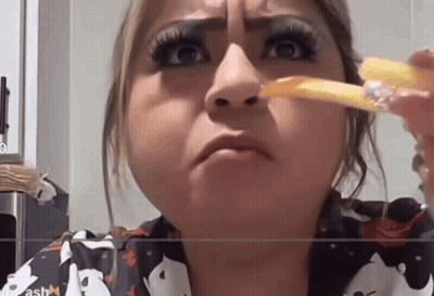 A Woman Is Eating French Fries And Making A Funny Face In Front Of A Screen That Says Ash GIF