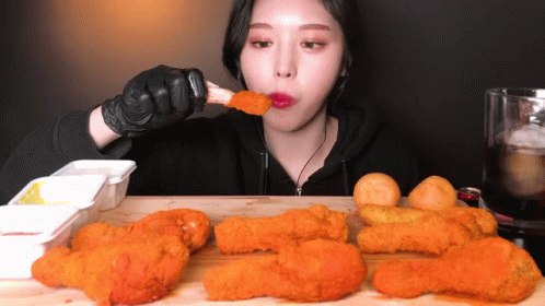 A Woman Is Eating Fried Chicken While Wearing Gloves GIF